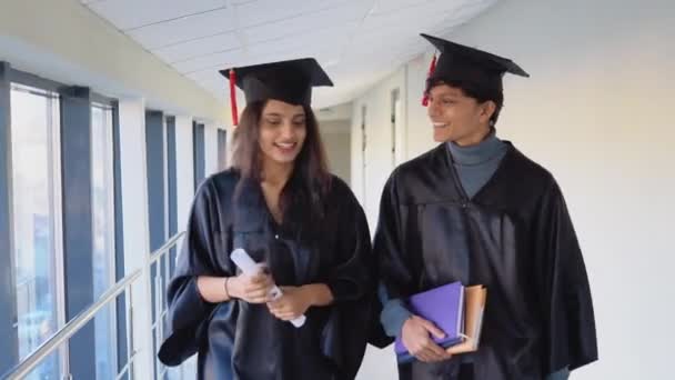 Dos indios graduados caminando por el pasillo de la universidad. Concepto educativo — Vídeos de Stock