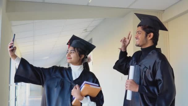Dos graduados indios se paran en un pasillo de la universidad y se toman una selfie. Concepto educativo — Vídeo de stock