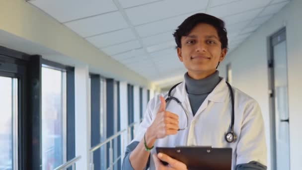 Friendly happy indian male physician or intern professional general practitioner posing with stethoscope looking at camera in clinic. Smiling young doctor close up portrait — Stock Video