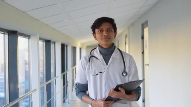 Indian male physician or intern professional general practitioner posing with stethoscope looking at camera in clinic. Smiling young doctor close up portrait — 图库视频影像