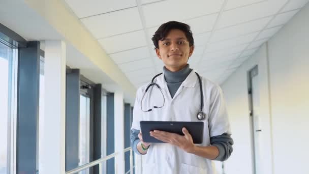 Indian male physician or intern professional general practitioner posing with stethoscope looking at camera in clinic — Stockvideo