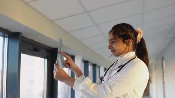 Female indian doctor examines x-ray of lungs, holding it in hands indoors — Stok video