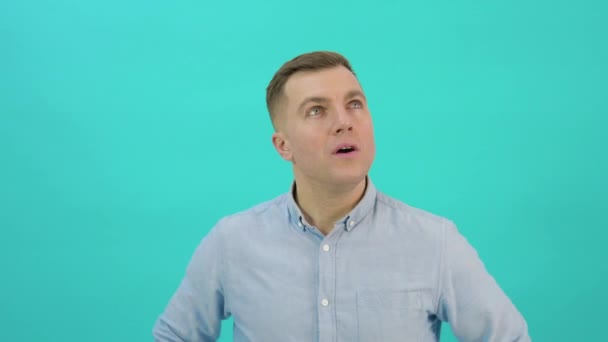 Studio portrait of confident caucasian man. A man in a blue shirt expresses bewilderment and indecision. Office worker standing in front of a bright blue background — Stockvideo