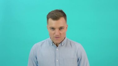 Caucasian middle-aged man in a blue shirt expresses anger, rage, aggressive shouting. Office worker standing in front of a bright blue background