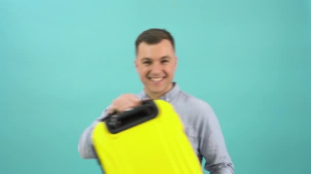 A Caucasian middle-aged man in a blue shirt expresses delight and joy with a yellow suitcase in his hands. An office worker is preparing for a vacation or business trip — стоковое видео