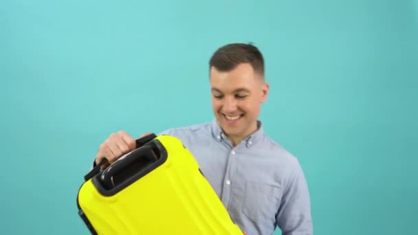 Happy positive man in a blue shirt happily shows off a stylish yellow plastic suitcase in his hands. Business man on a bright blue background — Stock Video