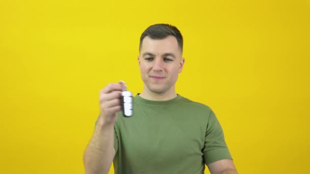 Caucasian middle-aged man in a green T-shirt happily shows a car key in his hand. Happy car owner, driver standing in front of yellow background — Stock video