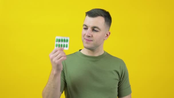 A man in holds two plates of different pills in his hands and expresses confusion. The guy is standing in front of a yellow background with drugs in his hands — Stockvideo