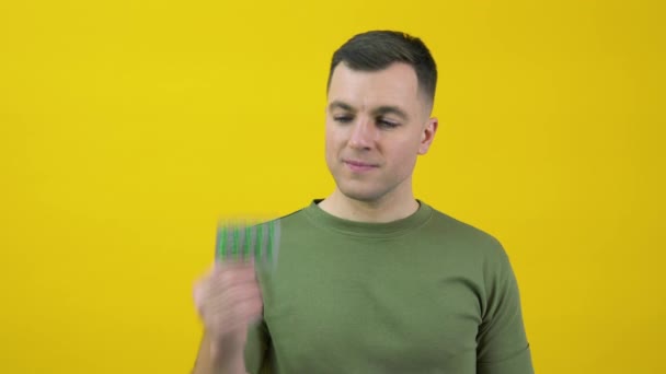 A man holds a plate of green capsules with drugs in his hands and expresses approval, consent, support, nodding his head. The guy is standing in front of a yellow background with drugs in his hands — Vídeo de Stock