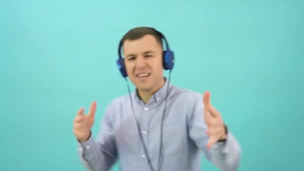 Caucasian middle-aged man in a blue shirt is having fun dancing in headphones. Cheerful office worker standing in front of a bright blue background — Video Stock