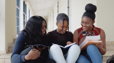 Bir grup Afrikalı Amerikalı öğrenci üniversitede kitaplar ve bir tabletle yerde oturuyor. Eğitim kavramı