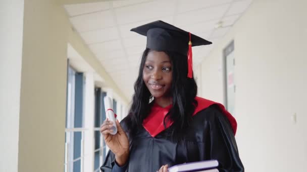 Mujer africana graduada en vestido negro y con sombrero de máster en la universidad. Un evento importante. Especialista joven. Graduado universitario de TI con diploma — Vídeos de Stock
