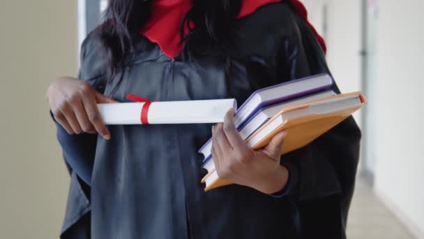 Une femme afro-américaine diplômée en manteau tient un diplôme et un livre entre ses mains. Gros plan. Éducation à l'étranger — Video