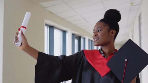 맨틀에서 졸업 한 아프리카 계 미국인 여성은 손에 졸업장을 쥐고 미소를 지으며 서 있습니다. 의대를 졸업하고 졸업장을 받다 — 비디오