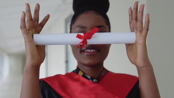 Eine Absolventin im schwarzen Kleid bedeckt seine Augen mit einem Diplom — Stockvideo