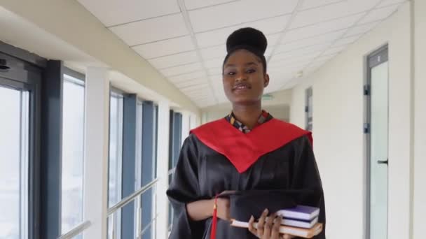 Femme afro-américaine diplômée en manteau se tient avec un diplôme dans les mains et sourit. Concept d'éducation en ligne — Video