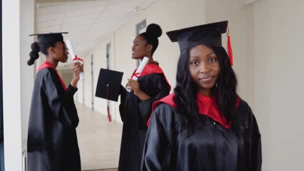 Una laureata gioiosa con un diploma in mano si trova all'università sullo sfondo di laureati che parlano tra loro — Video Stock