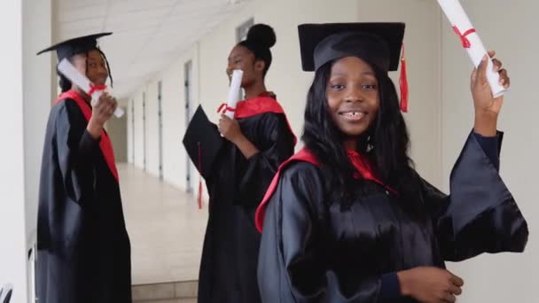 Μια χαρούμενη γυναίκα απόφοιτος με δίπλωμα στο χέρι στέκεται στο πανεπιστήμιο με φόντο τους απόφοιτους που μιλούν μεταξύ τους. Πρόγραμμα ανταλλαγής φοιτητών μεταξύ πανεπιστημίων ανά τον κόσμο — Αρχείο Βίντεο