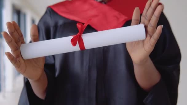 Afroamerykanka kończąca szkołę w płaszczu ma dyplom w rękach. Zbliżenie — Wideo stockowe