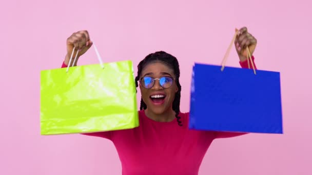 Schattig vrolijk jong Afrikaans Amerikaans meisje in roze kleren hebben plezier en dansen met papier gelamineerde tassen met handgrepen. tiener meisje staan op een solide roze achtergrond — Stockvideo