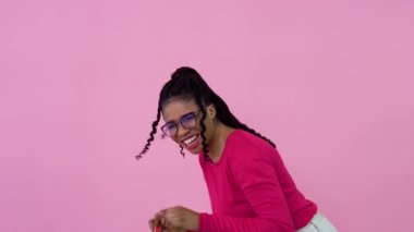 Şirin, neşeli, Afro-Amerikalı pembe elbiseli, elinde oyuncak bir alışveriş arabası tutan kız. Genç kız ev hanımı acemi, pembe arka planda duruyor.