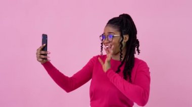 Pembe elbiseli tatlı Afrikalı Amerikalı kız video bağlantısıyla iletişim kuruyor. Pembe arka planda duran genç bir kız.