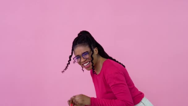 Schattig vrolijk jong Afrikaans Amerikaans meisje in roze kleren met een speeltje mini winkelwagentje. tiener meisje huisvrouw beginner staan op een solide roze achtergrond — Stockvideo