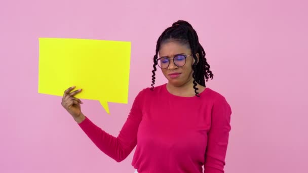 Carino giovane ragazza afroamericana si erge con manifesti per l'espressione su uno sfondo rosa solido. Un luogo per slogan pubblicitari — Video Stock