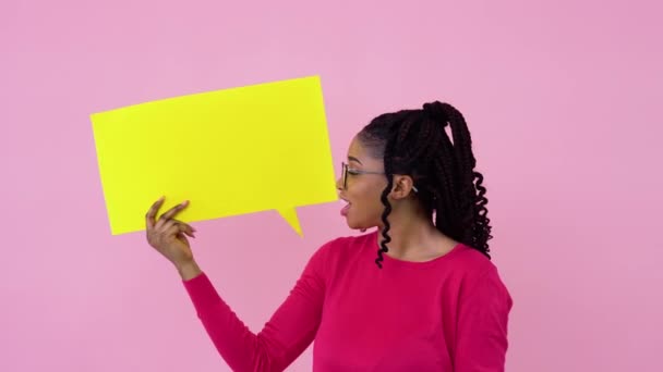 Menina afro-americana bonito jovem está com cartazes para expressão em um fundo rosa sólido. Um lugar para slogans publicitários — Vídeo de Stock