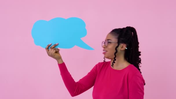 Jovem menina afro-americana em roupas cor-de-rosa está com cartazes para expressão em um fundo rosa sólido. Um lugar para slogans publicitários — Vídeo de Stock