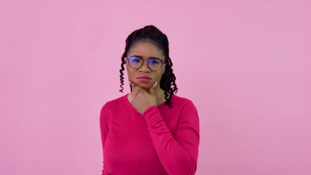 Roztomilá afroameričanka v růžových šatech se zamyšleně a vážně dívá do kamery. Dospívající dívka stojící na pevném růžovém pozadí — Stock video