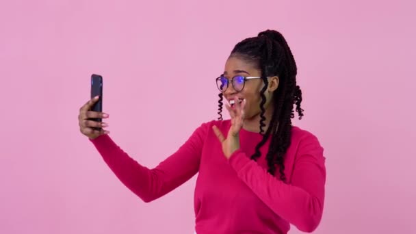 Carino giovane ragazza afroamericana in abiti rosa comunica tramite collegamento video. Teen ragazza in piedi su un solido sfondo rosa — Video Stock