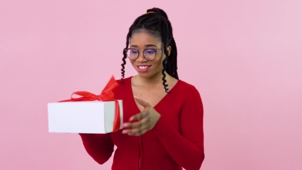 Chica afroamericana joven con ropa roja sosteniendo una caja blanca con cinta roja. Regalo de cumpleaños — Vídeos de Stock