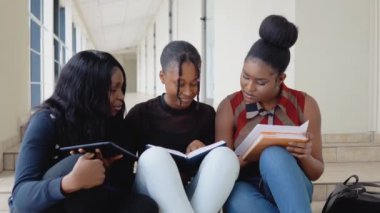 Bir grup Afrikalı Amerikalı öğrenci üniversitede kitaplar ve bir tabletle yerde oturuyor. Eğitim kavramı