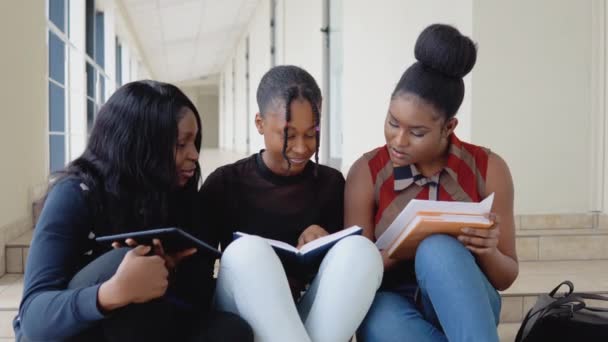 Eine Gruppe afroamerikanischer Studenten sitzt mit Büchern und einem Tablet auf dem Boden der Universität. Bildungskonzept — Stockvideo
