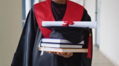 Manto mezunu Afrika kökenli Amerikalı kadın diploması ve elinde kitaplarla duruyor. - Yakın çekim. Yurtdışında eğitim