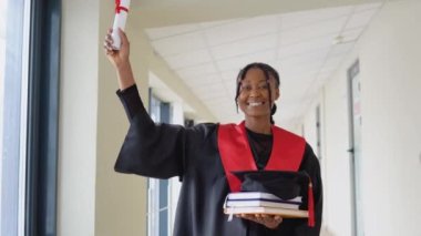 Afrika kökenli Amerikalı kadın mezunlar diploması ve ellerinde kitaplarla ve gülümsemeleriyle ayakta duruyorlar. Diplomalı bir ekonomi üniversitesi mezunu.