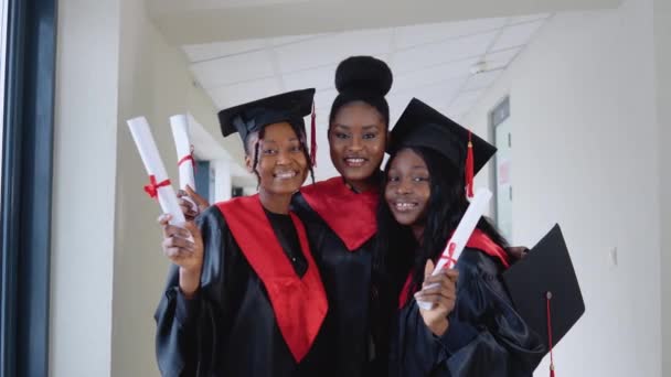 Mulheres universitárias afro-americanas graduadas ficam na frente da câmera em chapéus mestres e vestes pretas. Prosess de estudos universitários. Mestre em Ciências — Vídeo de Stock