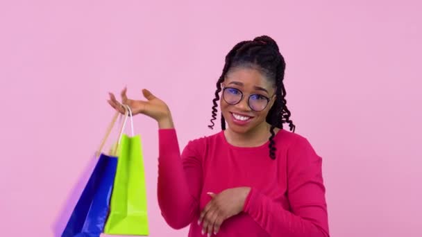 Jovem afro-americana em roupas cor-de-rosa se divertindo e dançando com papel laminado sacos com alças. Menina adolescente em pé sobre um fundo rosa sólido — Vídeo de Stock