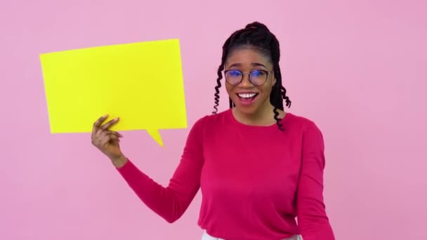 Joven afroamericana americana en ropas rosadas con carteles para la expresión sobre un fondo rosa sólido. Un lugar para consignas publicitarias — Vídeos de Stock