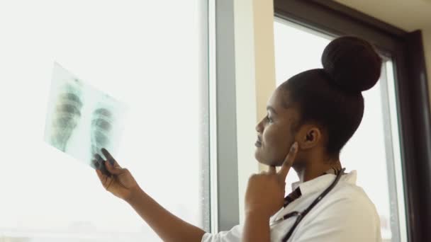 Női afro-amerikai orvos vagy gyakornok megvizsgálja a tüdő röntgenjét, és bent tartja a kezében. Specialist tartja átlátszó kép mellkas karok, és gondosan kutatja azt — Stock videók