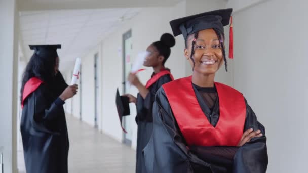 Una graduada alegre con un diploma en la mano se encuentra en la universidad en el contexto de los graduados que hablan entre sí. Programa de intercambio de estudiantes entre universidades de todo el mundo — Vídeos de Stock