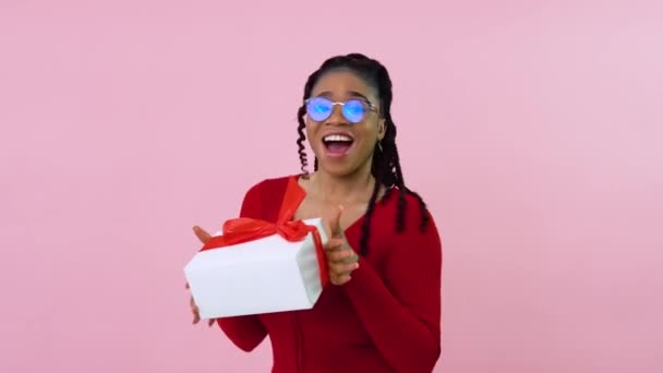 Carina ragazza afroamericana che balla con un dono. Studentessa in abiti rossi tiene una scatola bianca con un nastro rosso. Regalo di San Valentino — Video Stock