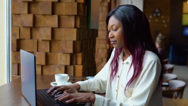 年轻的非洲裔美国女人在咖啡店里使用笔记本电脑。使用笔记本电脑的女性专业人员 — 图库视频影像