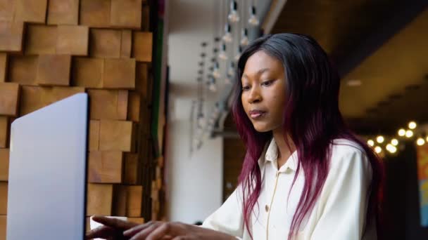 Mujer afroamericana joven usando computadora portátil en la cafetería. Profesional femenino trabajando con notebook — Vídeos de Stock