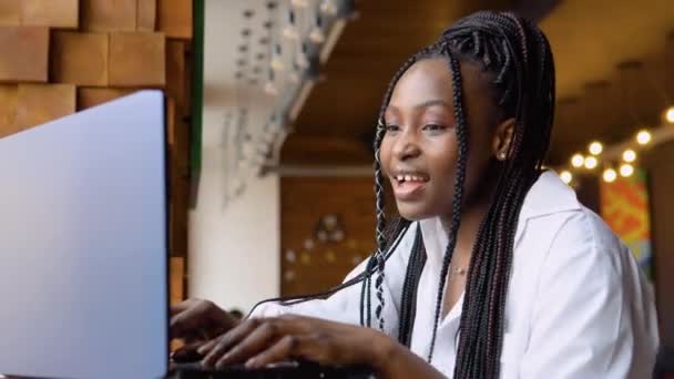 Νεαρή Αφροαμερικανή που χρησιμοποιεί φορητό υπολογιστή στο καφέ. Γυναικεία επαγγελματική εργασία με σημειωματάριο — Αρχείο Βίντεο