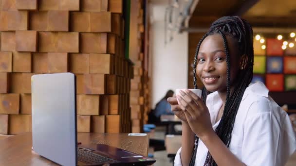 Young african woman drinking coffee and working on a laptop while sitting in a cafe — Stock Video