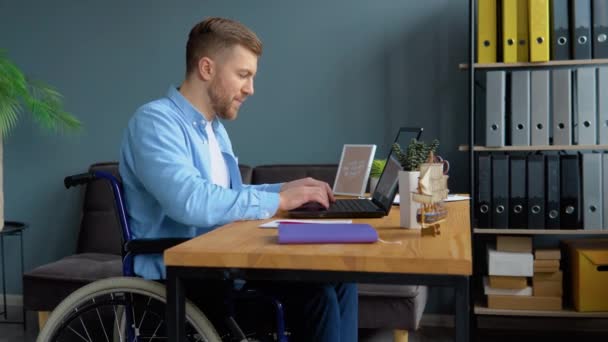 Мотивований фрілансер інвалідів працює з ноутбуком, який сидить у інвалідному візку в офісі. Дистанційна робота та концепція інвалідності — стокове відео