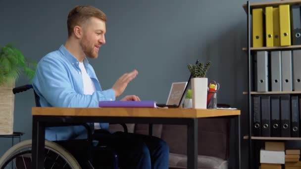 Motiverad glad handikappad frilansare som pratar i videochatt medan han sitter på kontoret i rullstol — Stockvideo