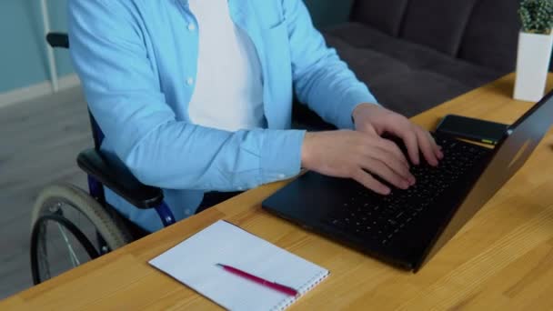 Estudiante masculino aprendiendo en línea usando computadora portátil escribiendo sentado en silla de ruedas en un apartamento ocupado con la educación a distancia. Concepto de inclusión y discapacidad — Vídeo de stock